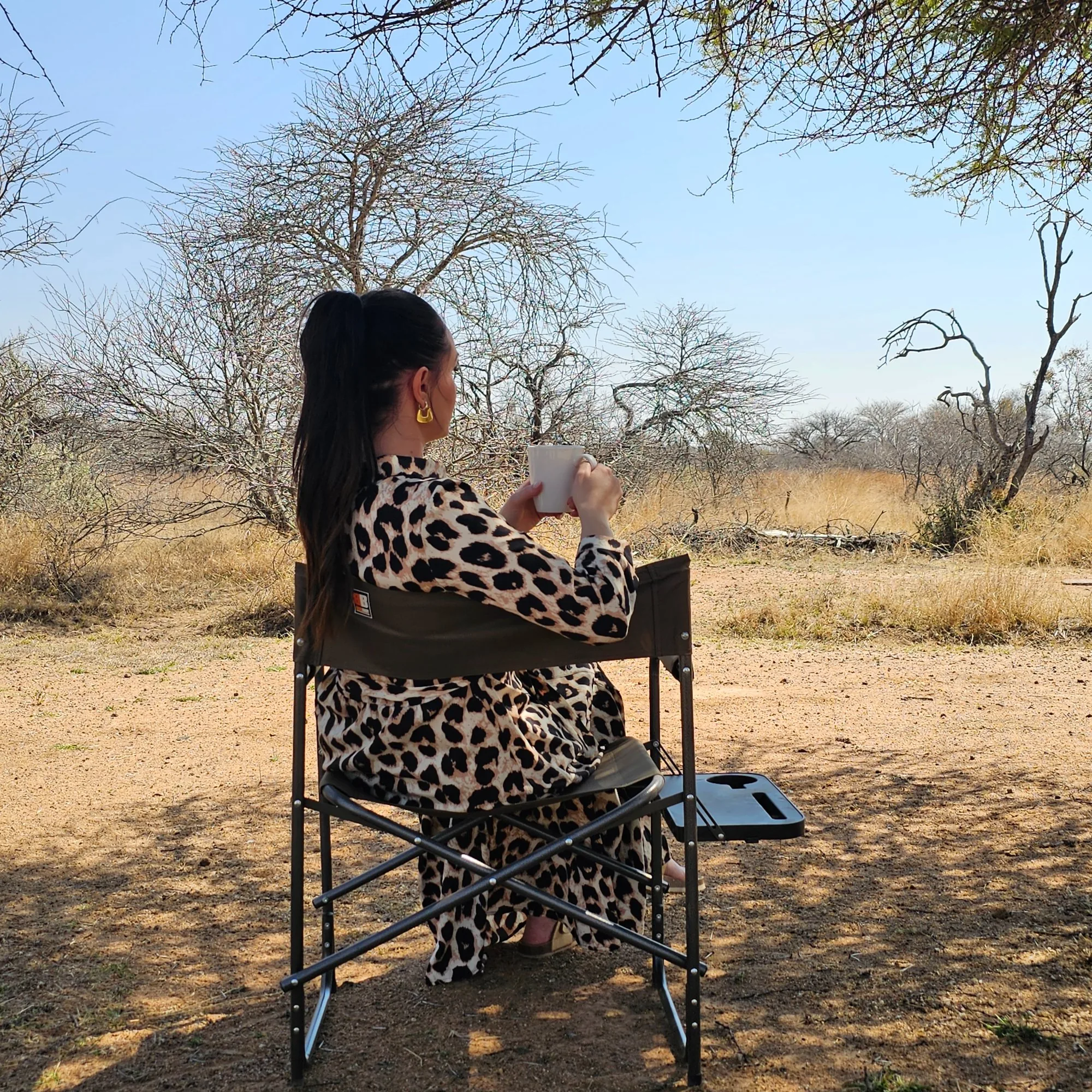 A guest in a camp chair holding a coffee mug, looking out over open bushveld grassland