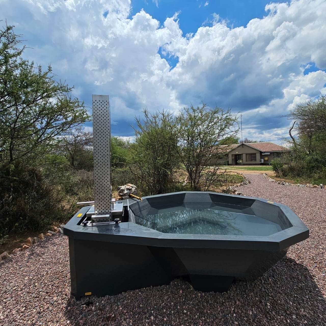 Wood-fired hot tub filled with water, set on gravel with the lodge visible behind