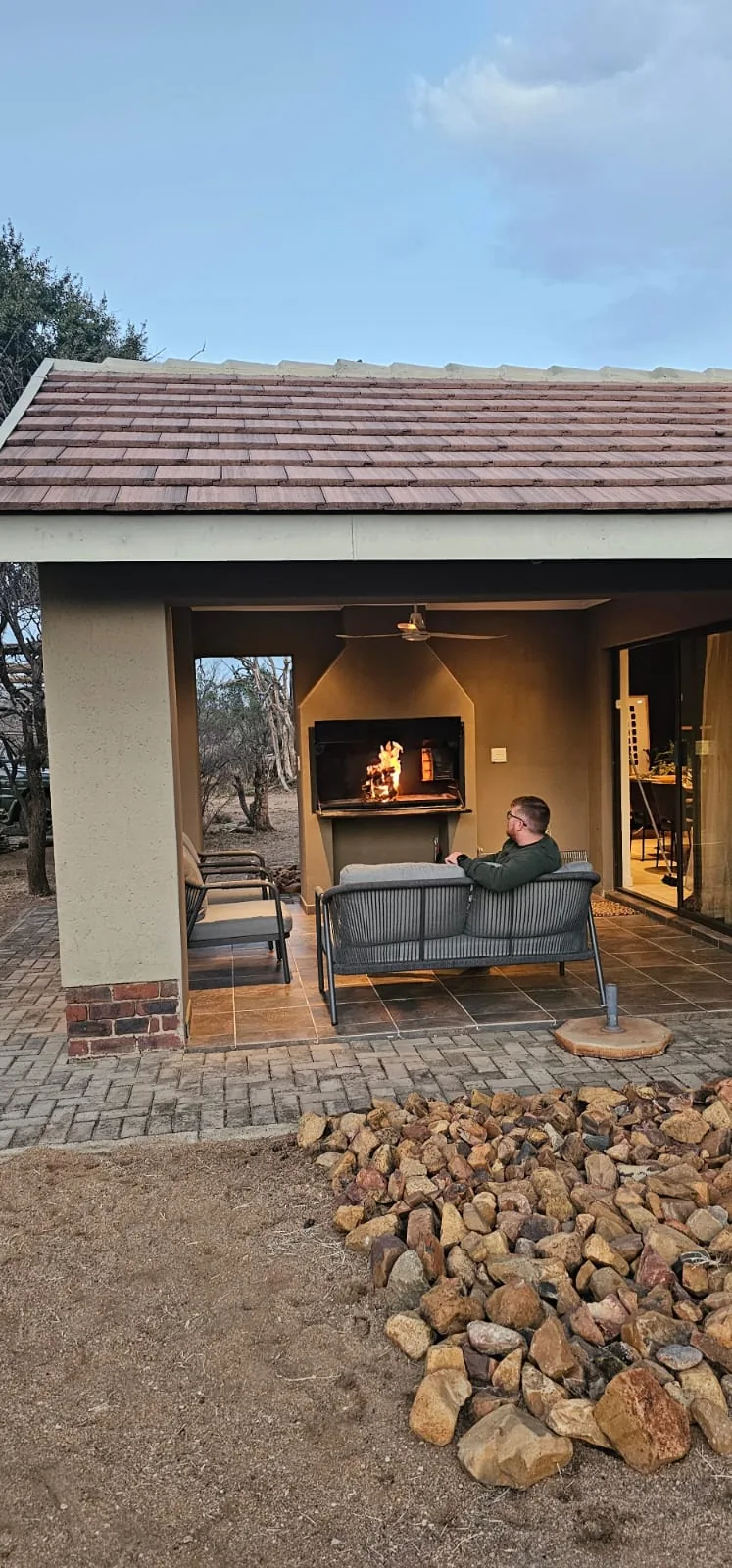 Covered patio with a lit built-in braai and outdoor seating in the evening