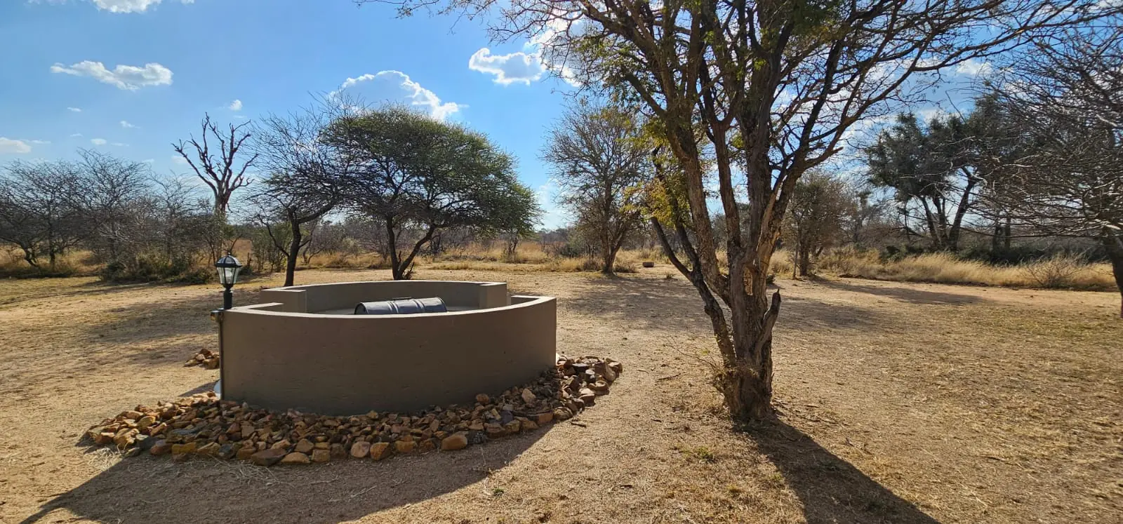 The outdoor boma firepit wall, unlit, surrounded by bushveld trees