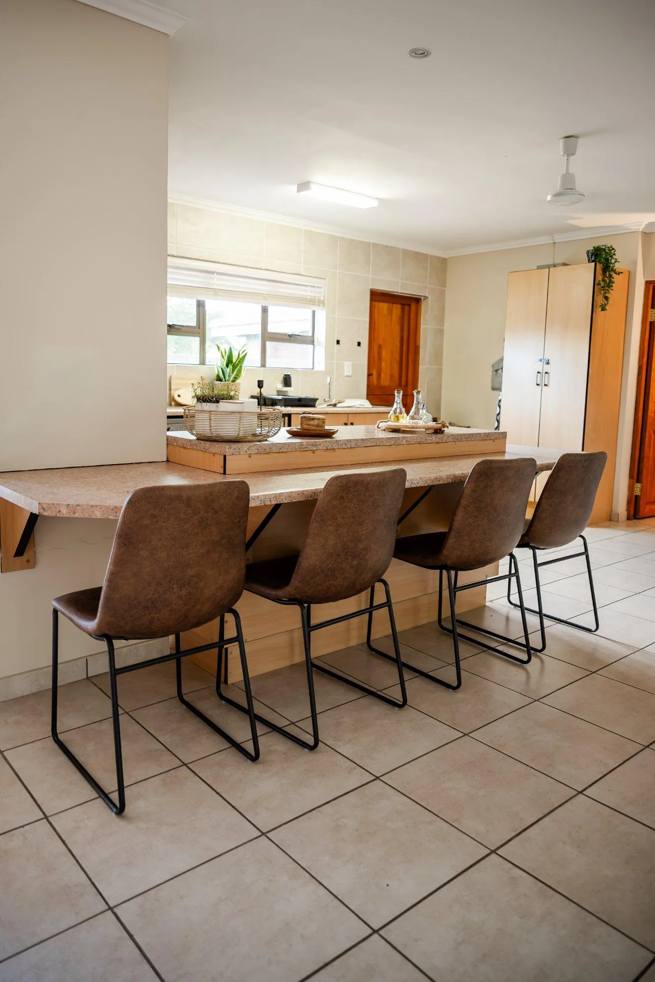 Kitchen counter with four brown leather bar chairs, looking through to the kitchen