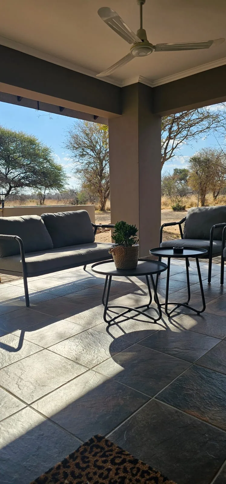 Covered patio with a grey outdoor lounge suite and a ceiling fan, looking out at the bush