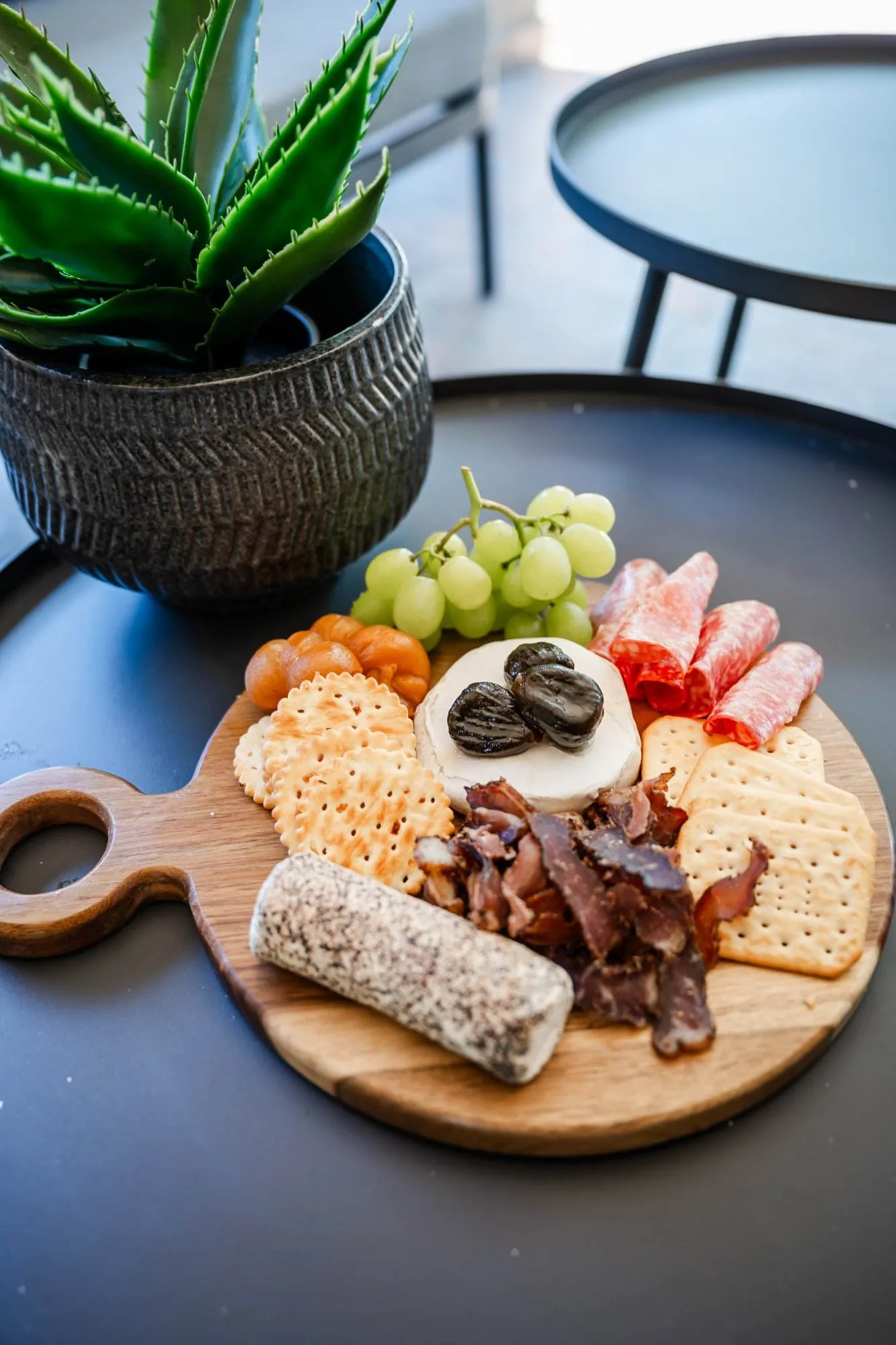 A cheese and charcuterie platter with grapes and crackers on a round wooden board