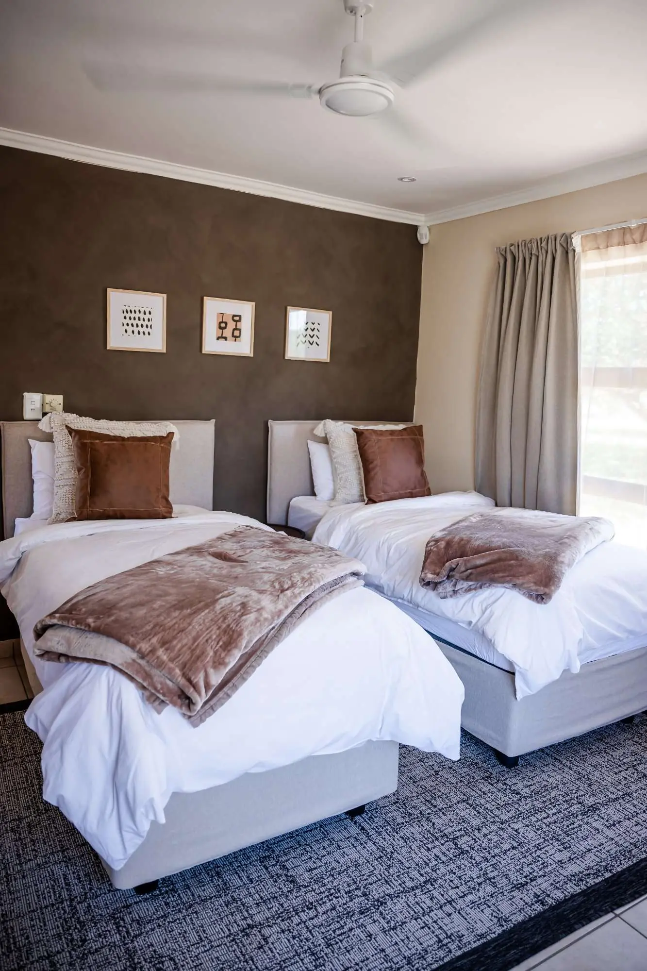 Second bedroom with twin beds, a warm brown feature wall and framed art prints